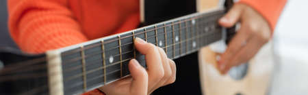 cropped view of young woman playing acoustic guitar at home, banner