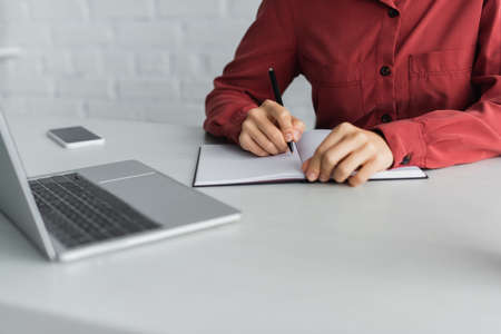 cropped view of teacher writing in notebook near devices on deskの写真素材