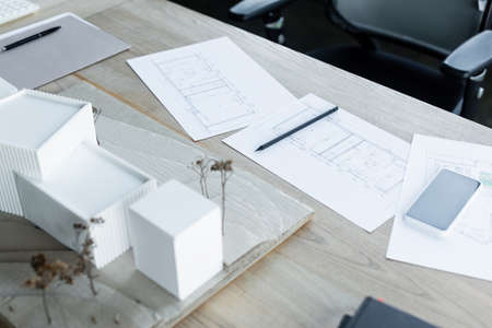 architectural plans near blurred house models and mobile phone on wooden desk in office