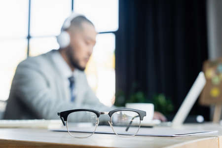 selective focus of eyeglasses near blurred asian businessman working in office