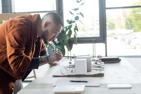 asian engineer pointing with pencil at house models while working in architectural bureauの写真素材