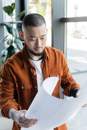 asian architect looking at blueprint while working in officeの写真素材