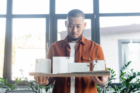 asian architect holding construction project with house models in office