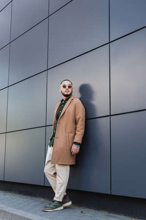 full length view of asian man in stylish autumn outfit and sunglasses near grey wall in cityの写真素材