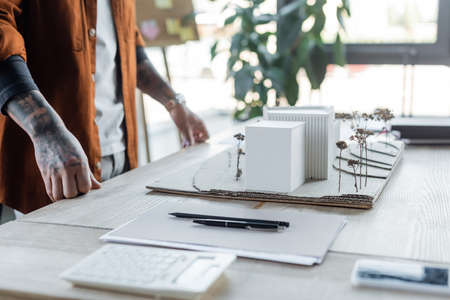 cropped view of architect standing near work desk with house models, folders and blurred calculatorの写真素材