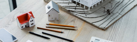 high angle view of pencils, house models and smartphone on wooden desk, bannerの写真素材