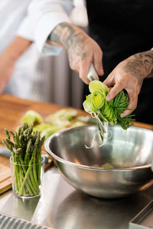 Cropped view of chef holding sliced leek and knife near bowl and asparagus in kitchenの写真素材