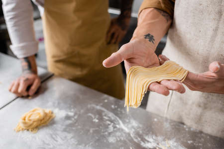 Cropped view of chef holding raw spaghetti near colleague in kitchenの写真素材