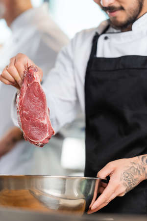 Cropped view of tattooed chef holding raw meat near bowl in kitchenの写真素材