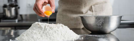 Cropped view of chef pouring egg yolk on flour on table, banner