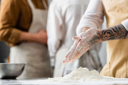 Cropped view of tattooed chef standing near flour on table in kitchen
