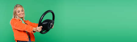 happy woman in orange jacket holding steering wheel isolated on green, bannerの写真素材