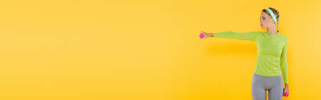 slim woman in sportswear training with dumbbells isolated on yellow, bannerの写真素材