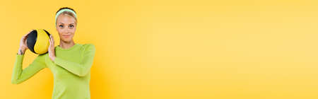 smiling sportive woman with ball looking at camera isolated on yellow, bannerの写真素材