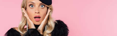 thrilled blonde woman with open mouth looking at camera while touching face isolated on pink, bannerの写真素材