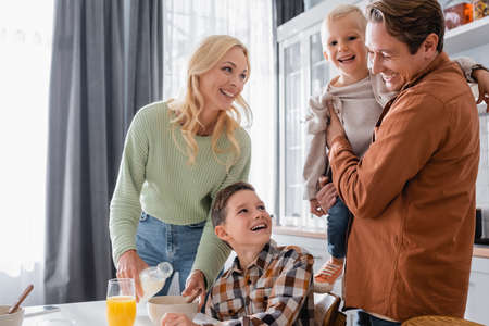 woman pouring milk into bowl near family in kitchenの写真素材