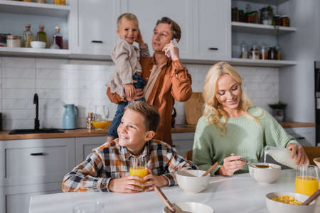 man holding kid and pouring milk in corn flakes during breakfast in kitchenの写真素材