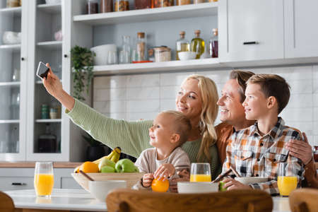 happy woman taking selfie on mobile phone while having breakfast with family