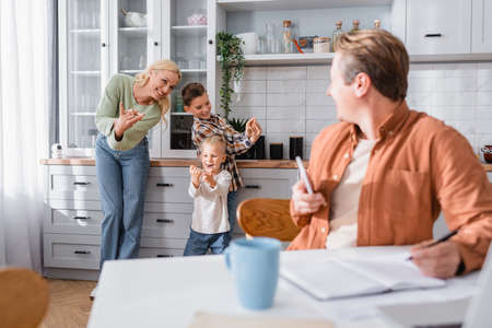 cheerful woman playing in kitchen with sons near husband working on blurred foregroundの写真素材