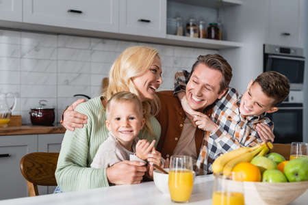 pleased parents and sons embracing during breakfast near orange juice and fresh fruitsの写真素材