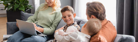happy dad and sons sitting on couch near woman working on laptop, banner