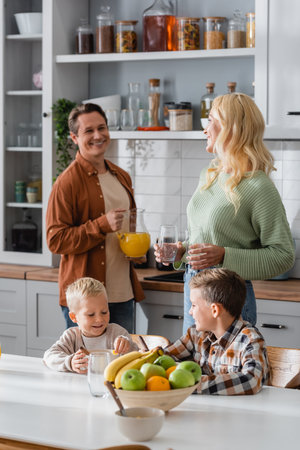 brothers eating breakfast near blurred parents with glasses and orange juiceの写真素材