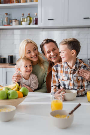 cheerful parents embracing kids while having morning breakfast in kitchenの写真素材