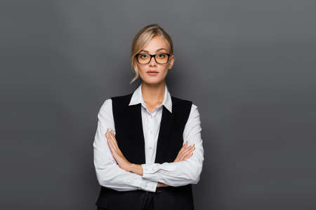 Pretty businesswoman standing with crossed arms and looking at camera isolated on grey