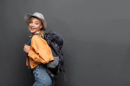 Positive tourist with backpack and hat looking away isolated on greyの写真素材