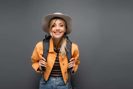 Pretty blonde tourist with backpack looking at camera isolated on grey