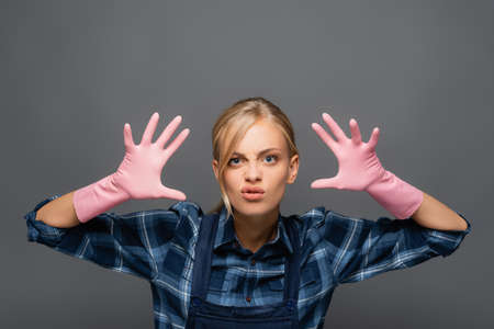Disgusted plumber in rubber gloves gesturing and looking at camera isolated on greyの写真素材