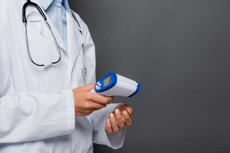 Cropped view of doctor holding non contact pyrometer isolated on grey