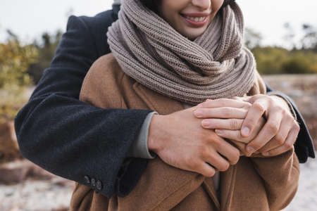 partial view of man hugging smiling woman in autumn coat and scarf outdoors