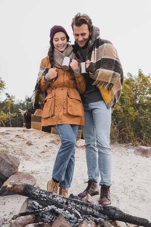 smiling tourists in autumn outfit standing with thermo cups near bonfireの写真素材