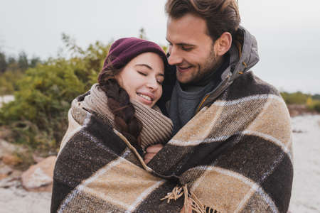 happy young couple warming in checkered blanket outdoorsの写真素材