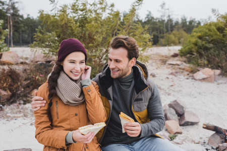 smiling man embracing girlfriend while eating sandwiches during haltの写真素材