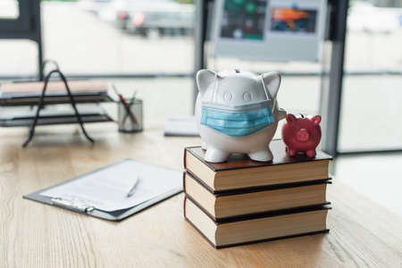 piggy banks with medical mask on codex books near blurred contract on desk, anti-corruption conceptの写真素材