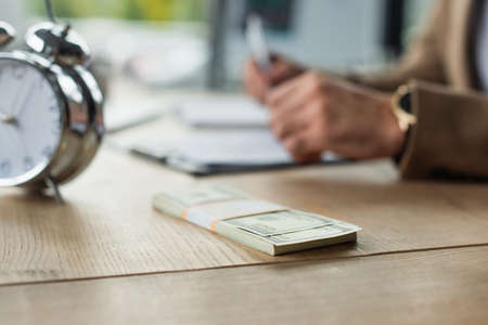dollar banknotes near alarm clock and cropped businessman on blurred background, anti-corruption...