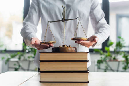 cropped view of businesswoman near justice scales on books in office, anti-corruption concept