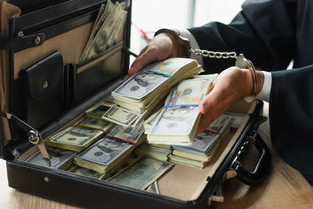 partial view of businessman in handcuffs holding dollars near briefcase, anti-corruption conceptの写真素材
