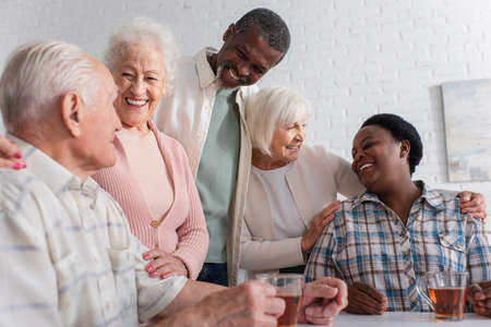 Positive interracial friends talking near tea in nursing homeの写真素材