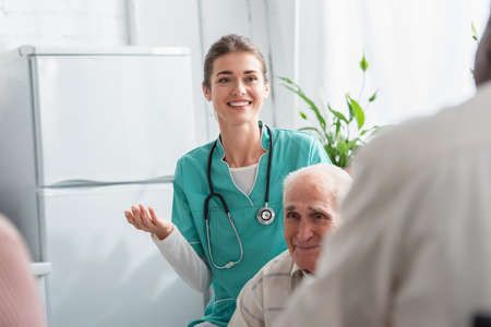 Positive nurse with stethoscope near interracial senior patients in nursing homeの写真素材
