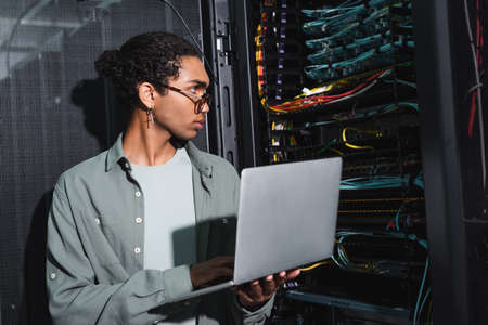 african american engineer holding laptop while looking at wires in serverの写真素材