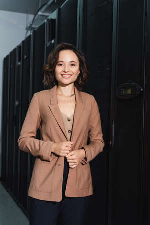 cheerful engineer smiling at camera while standing in data center