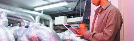partial view of afican american engineer with digital tablet and paper cup in technical equipment...