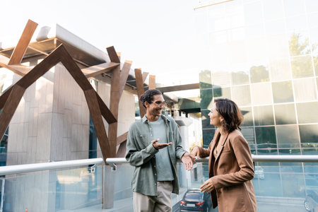 smiling african american man pointing with finger while talking to woman on balcony outdoors