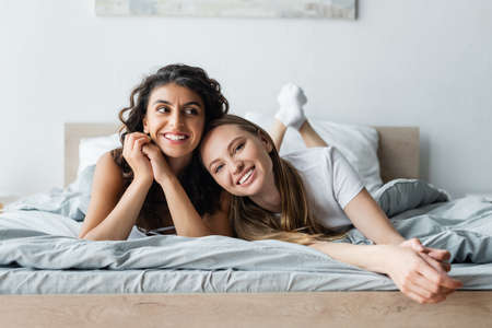 smiling lesbian couple lying on bed at home