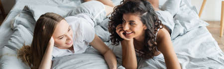 joyful lesbian women lying and holding hands on bed, bannerの写真素材