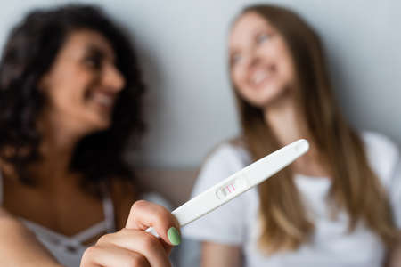 blurred and cheerful woman holding pregnancy test near happy girlfriendの写真素材