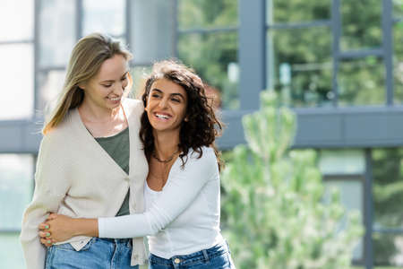 curly woman smiling while hugging girlfriend outsideの写真素材